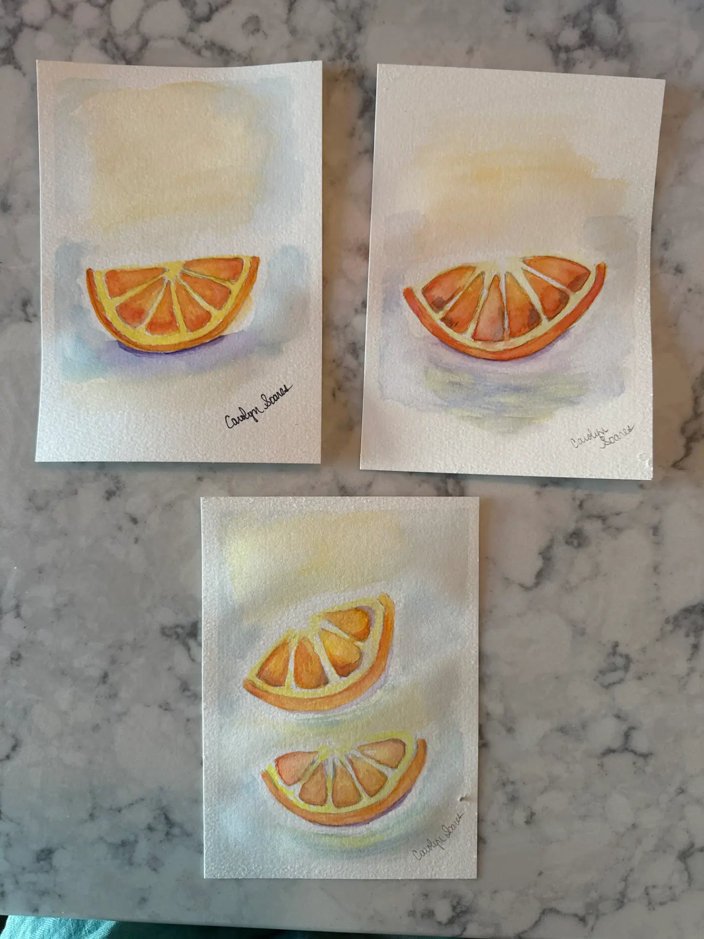 Three student watercolour orange slice studies on watercolour paper