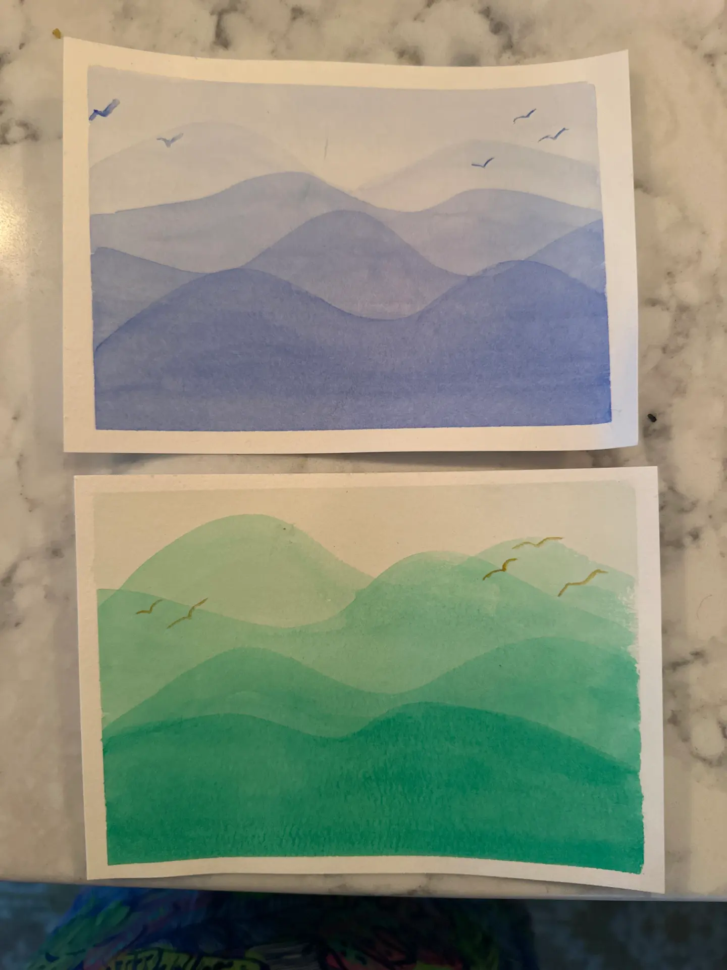 Two student watercolour layered hill landscapes in blue and green with birds